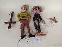 Both vintage marionettes laid flat showing entire puppets with control bars and strings.