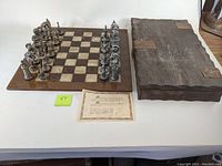 Chessboard fully set up with metal chess pieces and wooden storage box closed beside it, certificate placed on table