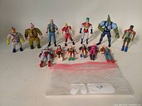 Full view of 15 mixed action figures from various series including Captain Planet and TMNT laid on table with small plastic bag.