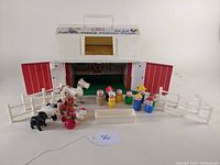 Full view of Fisher Price white barn with red doors, Little People figures, animal figures, white fences, and trough arranged in front.