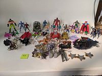 Overview photo showing a large variety of mixed action figures and accessories including Batman figures, fantasy characters, vehicles, and various small toys grouped together on a table.