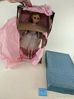 Photo showing the vintage 16-inch Elisa Madame Alexander doll in original box wrapped in pink tissue paper alongside the blue box.