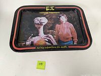 Top-down view showing the printed image of E.T. and Elliot, with text on black tray surface and red border.