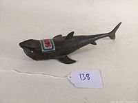 Side view of dark gray plastic shark figure with visible fins and tail, showing "Official Jaws" sticker on top side