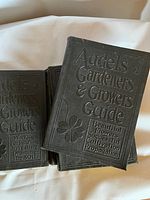Close up of two of four hardcover books with black canvas embossed covers titled Audels Gardeners and Growers Guide with floral motifs.