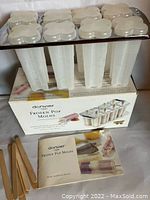Set of eight white flower-shaped popsicle molds with caps stacked on original box, instruction booklet and wooden sticks shown on box surface.