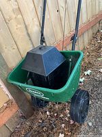 Green Scotts Speedy Green 1000 fertilizer spreader shown along fence with black bug zapper placed inside the spreader hopper.