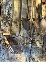 Gardening tools arranged on a weathered wooden surface including shovels, rakes, and hoe showing wear and use.