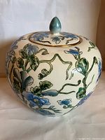 Full view of the ginger jar showing blue flowers and green vines with the lid in place against a neutral background.