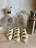 Photo showing all items: Russian liquor bottle, 11 white ceramic escargot pots, snowman glass plate, and Magnum cream canister