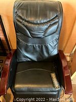 Front view of Takasima massage chair showing black faux leather cushioning and removable wooden armrests with red lacquer finish. Remote control visible on seat.