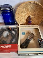 Photo shows a blue glass jar with metal clasp lid, round woven basket, Koss TV headphones in box, and flashlight multi-tool in box.