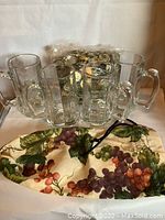 Four clear glass beer mugs arranged upright, with a grapevine printed wine gift bag and an unused tote bag.