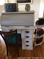 Front angled view of the white wooden roll top desk with chair in front, showing the roll top closed and books on top.