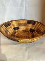 Side view of the shallow coiled basket showing the natural and dark dyed fiber pattern and basket shape.