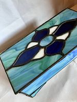 Close-up of stained glass lid showing blue, turquoise and white glass pieces arranged in a floral or geometric pattern with soldered edges.