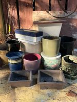 Various ceramic and pottery plant pots arranged outdoors on a table, showing shapes and colors of each.