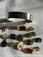 Full view of the Indigenous-themed silver-tone cuff bracelet along with a variety of vintage pins arranged on white fabric.
