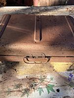 Closed view of rusty metal box-style camp stove showing carrying handle and secured latch.