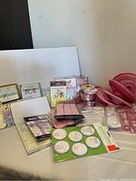 Photo shows boy and girl baby shower invitations, pink paper lanterns, thank you cards, pink ribbon rolls, and shower party buttons on a white surface.