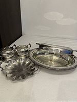 Silver plated casserole dish with lid and glass liner alongside candy dish and cream and sugar set on tray.