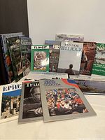 Photo showing group of 13 books and magazines arranged standing and lying down, including titles on gardening, regional history, cultural topics.