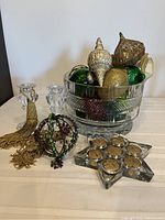 Clear cut glass bowl filled with assorted Christmas ornaments. Display includes two clear glass candle holders, a star-shaped candle holder with gold tea lights, two gold tassels, and a metal ornament with gold and green glass.