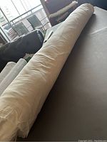 Roll of beige drapery lining fabric laid on a table showing the full length rolled tightly.