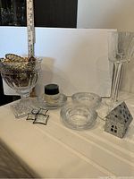 Photo showing glass bowl on pedestal filled with glass pinecones, two tall glasses, three round glass candle holders, small tin house candle holder, and a small glass angel figurine.