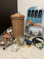Full lot showing wicker toilet paper holder, two metal cake pans, crystal Darques picture frame, candle holder, shopping bags, cookie ornament, and bathroom glass holder