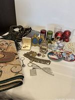Overview photo showing costume jewelry pieces, Christmas decorations, green tassels, gold green Christmas runner folded in fabric, and other small items on table.
