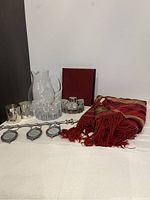 Overview of glassware, silver candle holders, photo album, throw, and Bombay frame arranged on white cloth