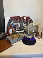 Full view of all items in the lot arranged on table: clothing, frames, box of hair accessories, horse bookend, toothbrush holder, photo clutch, and letter folder.