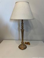Full view of the table lamp showing beige cloth-covered shade and gold-coloured molded resin base, approximately 28 inches tall.