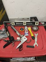 Tools including caulking guns, level, wrench, tape measure, glue, scraper on red surface