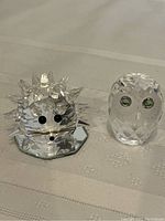 Two Swarovski crystal figurines: hedgehog with spikes and owl with green eyes on mirror base.