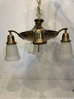 Full view of the chandelier showing three white floral glass shades and one missing shade, brass and copper finish with decorative elements.