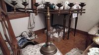 Full view of the brass candle holder placed on a floral fabric covered table, with three horizontal arms for candles and a central stand.