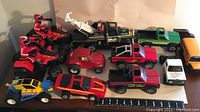 View of all eleven Buddy L toy vehicles including police tow truck, red pickups, motorcycles, and various cars lined up with ruler for scale