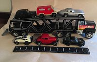 Side view of car carrier with six cargo cars spaced on and in front of trailer, ruler shows size scale
