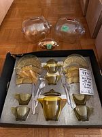 Set of glass tea party items and three clear piggy banks on cardboard and foam surface.
