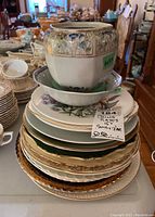 Stack of various decorative china plates with a shallow bowl and a ceramic jar on top, showing detailed patterns.