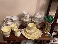 Full view of china sets including Royal Albert Pastella in yellow and additional unmarked white/gold floral pieces.