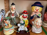Photo showing the three clown figurines including the music box, musical bust, and turnkey figure on a shelf with visible wear and paint chips.