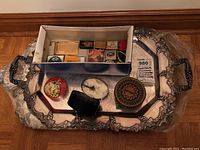 Top-down view of two silverplate Sheffield reproduction trays holding various vintage compacts, pill boxes and miniature cases along with a small address book.