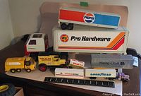Nine vintage toy trucks displayed with a ruler for scale, showing various corporate logos including Pro Hardware, Pepsi, Shell, Hapag-Lloyd, Goodyear, and American Airlines.