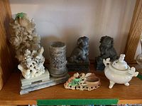 Shelf view showing floral bird carving with cylindrical brush pot on shared rectangular base, brush rest, grey foo dog pair and porcelain censer