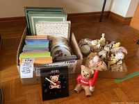 Overall view showing boxes with photo albums and collectible plates, as well as a collection of figurines including Avon and Precious Moments pieces.