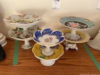 Set of six compotes displayed on wooden surface, showing varied decorative patterns and styles including floral and grape motifs.