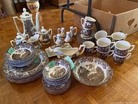 Photo showing full set of serving ware items arranged including bowls, plates, cups, teapot, condiment containers with brown romantic countryside design.